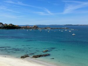 Corpus Christi Marks Milestone: Coastal harbor with turquoise water, anchored sailboats, a pier, and red-roofed buildings under a bright blue sky.