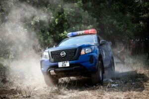 Former Corpus Christi Officer case highlights as a police vehicle drives through dusty terrain near a wooded area with bystanders nearby.