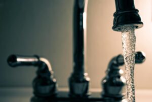 Close-up of running tap water with chrome faucet handles in soft lighting, symbolizing water access and conservation as Texas invests $20B.