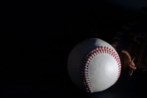 Close-up of a baseball with red stitching lit dramatically against a dark background, featuring a glove in the shadows; Astros vs Angels recap.