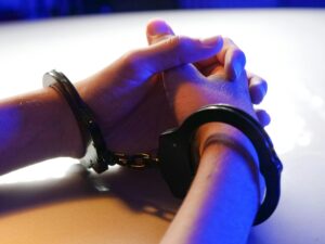 Hands in handcuffs under blue lighting, symbolizing law enforcement action — CCPD Officer Arrested in connection with an indecent assault case.