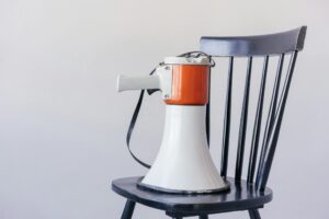 Civil Rights Complaint Over Corpus: A white and orange megaphone sits on a black chair, symbolizing protest and public advocacy.