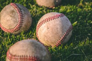 Astros Welcome Back Cristian Javier – close-up of worn baseballs with red stitching resting on green grass in sunlight.