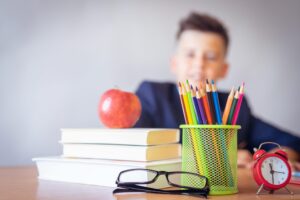 Back-to-School Brings Nerves with colorful pencils in a green holder, stacked books with an apple, glasses, and a red alarm clock.