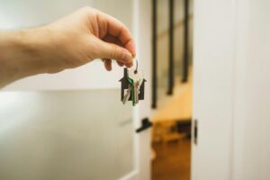 A hand holding house-shaped keychain and keys in front of a home entrance; Corpus Christi Launches Major housing initiative.