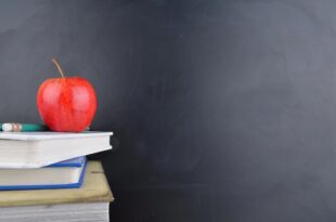 A red apple and pencil rest on stacked books in front of a chalkboard, symbolizing education progress as Corpus Christi schools rise.