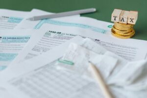 A New Tax Rate. A close-up of tax forms, a pen, and a stack of coins with blocks spelling "TAX" on top.