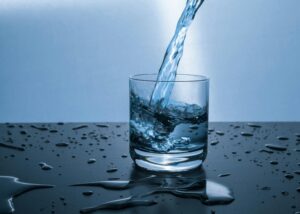 Corpus Christi's Water Future: Water pours into a clear glass, with splashes and droplets on a dark, reflective surface.