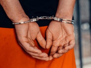 Close-up of a man in orange prison pants with his hands cuffed behind his back, symbolizing Rockport Man arrested for child.