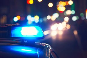 Blue police lights flash on a patrol car at night with blurred city lights in the background during a Downtown Corpus Christi shooting scene.
