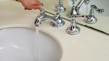 A person turns on a chrome faucet with running water in a bathroom sink, symbolizing water access as Corpus Christi drops plan.