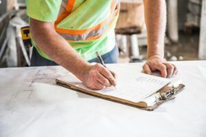 Construction worker writing on clipboard over bridge project plans, Farewell to an Icon, planning and safety on site.