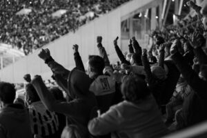 Houston Texans win: A crowd of excited fans in a stadium stands and cheers with raised fists during a football game celebration.