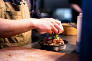 Chef preparing gourmet dish at New Texan Gas and Gourmet, highlighting fresh, made-to-order meals for Corpus Christi travelers.
