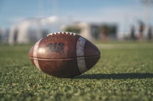 A Wilson football rests on the green turf under clear skies, symbolizing UNT Football Sellout excitement before the big game.