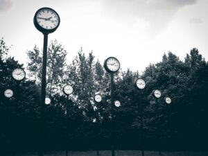 Multiple outdoor clocks on tall poles showing different times, symbolizing global time shifts and Why Daylight Saving Time.