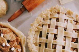 Homemade apple pies with lattice crusts and baking tools on a kitchen counter, showcasing fall flavors. Best Corpus Christi Pies.