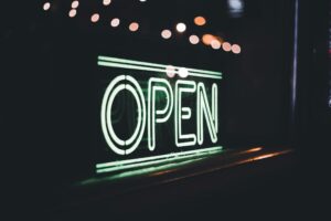 Neon green “OPEN” sign glowing in a dark storefront window, highlighting extended Black Friday store hours.