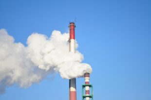 Industrial chimneys releasing white smoke under a clear blue sky, symbolizing air emissions and Cheniere Energy Pollution.