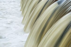 Close-up view of water cascading over a spillway, showing smooth flowing streams and white foamy currents below.
