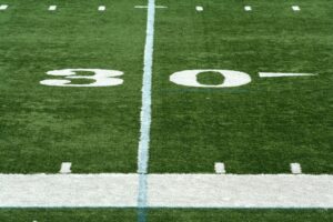 Close-up view of a football field showing the 30-yard line marker, white yard markings, and green turf under bright daylight.