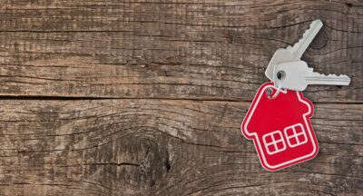 House keys with red home-shaped keychain on a rustic wooden surface, symbolizing real estate, home buying, and property ownership.