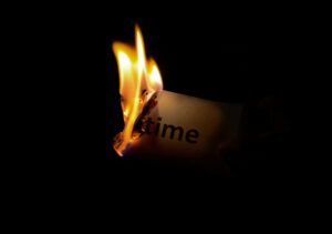 Burning paper with the word “time” caught in flames against a dark background, symbolizing deadline or loss.