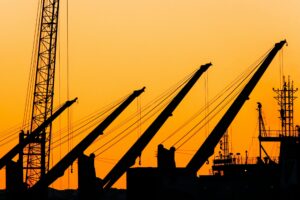 Silhouetted port cranes and cargo equipment at sunset, representing industrial operations at the Port of Corpus Christi.