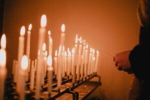 Hands light candles on a menorah during a Hanukkah vigil, symbolizing remembrance, mourning, and solidarity after tragedy.