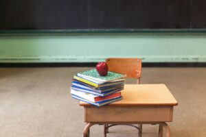 Stack of school books topped with an apple on a student desk in an empty classroom, representing education in Corpus Christi ISD.