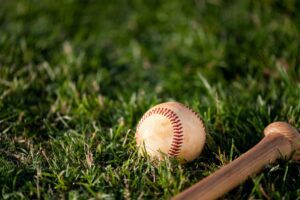 A baseball resting on green grass beside a wooden bat, symbolizing America’s pastime and the start of a baseball game. Tatsuya Imai