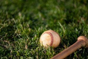 Baseball resting on green grass beside a wooden bat on the field, symbolizing America’s pastime and the start of a game.