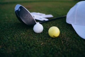 Golf driver, white and yellow balls, glove and cap on grass during Andrea Pavan injury coverage story.