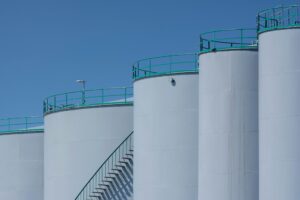 Thinking about creating concise alt text incorporating Trump Port of Corpus Christi referenceLarge white oil storage tanks with green railings at Trump Port of Corpus Christi under a clear blue sky.