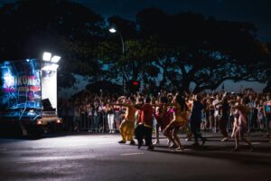 Dancers perform in vibrant costumes during Buc Days Rally Night Parade as a lit float and crowd line the street at night
