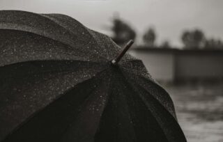 Close-up of a rain-soaked black umbrella under light rainfall with blurred background, illustrating Coastal Bend weather conditions