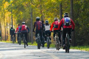 Group of cyclists riding together on a tree-lined road during a memorial ride honoring Ronnie Mathis in daylight