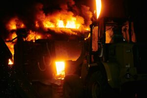 Grain elevator explosion engulfs industrial machinery in flames as heavy equipment operates amid intense fire at night