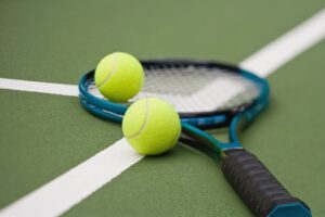 Close-up of two tennis balls resting on a racket on a green court, symbolizing Houston Cougars tennis training and match play