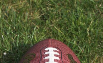 Close-up of an American football resting on green grass field in daylight, symbolizing NFL action and Will Anderson Jr contract