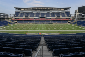 Empty stadium seating overlooking a football field during daytime, representing Houston sports venue development.
