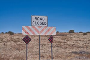 Road closed sign with barricade and reflectors on rural highway under blue sky, symbolizing SH 44 closures in Corpus Christi