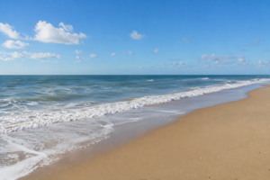 Sunny beach shoreline representing piggy banks and marine debris along coastal waters.