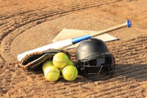Softball bat, glove, balls, and helmet on a field, illustrating youth sports amid child grooming charges investigation.