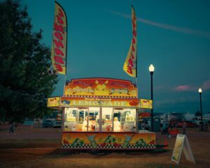 Lemonade Day Coastal Bend stand glows at dusk as visitors gather around a colorful lemonade booth at a community fair.