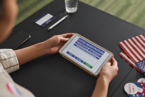Person using a tablet for voter registration beside U.S. flags during the Texas Democratic Convention in Corpus Christi.