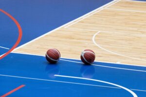 Two basketballs rest on a blue indoor court, representing Will Guillory's new role covering the Houston Rockets beat.