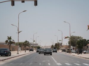 Vehicles travel along a palm-lined road with security vehicles ahead, illustrating traffic preparations for Donald Trump’s Corpus Christi visit.